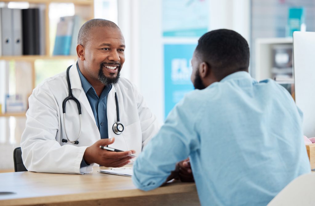 Happy, talking and doctor with a black man for healthcare, support and advice on treatment.